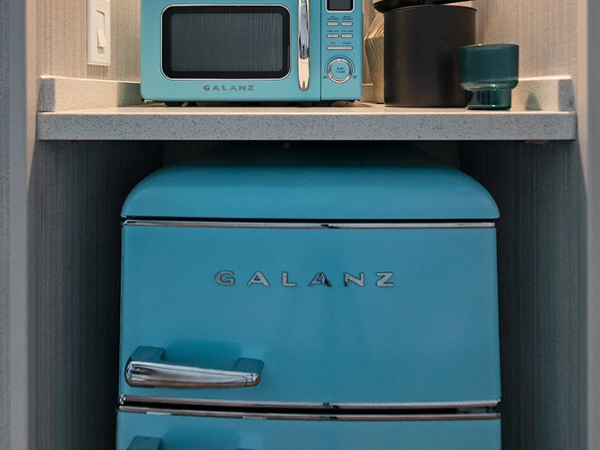 A retro turquoise GALANZ fridge with a matching mini toaster oven on a shelf above, and colorful decor including flowers in a pot.