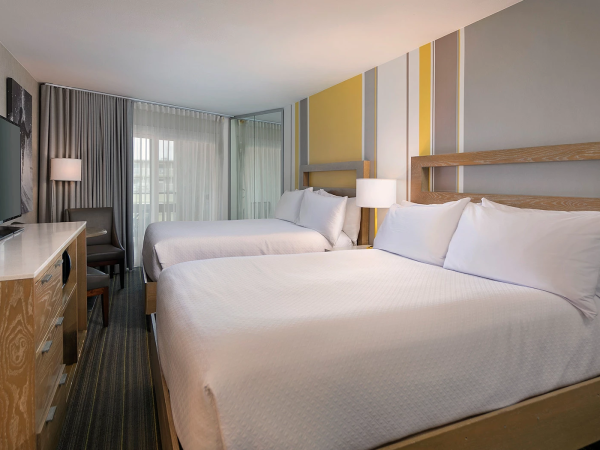 A hotel room with two queen beds, a desk, flat-screen TV, lamps, and a window with curtains. End.