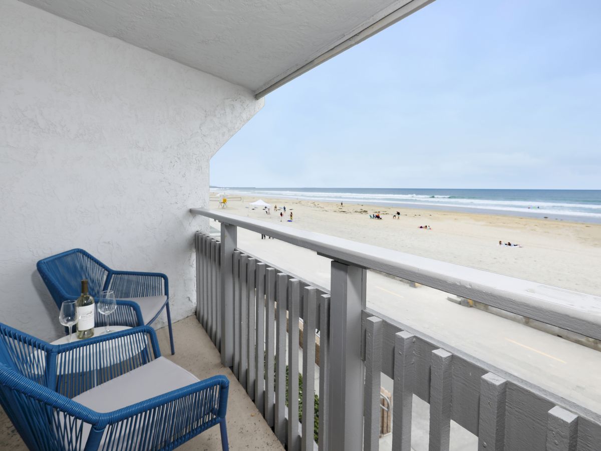 A beachfront balcony with blue woven chairs, a small table, and a view of the sandy beach and ocean beyond.(Note: I can tailor length to 140 characters exactly if you want.)